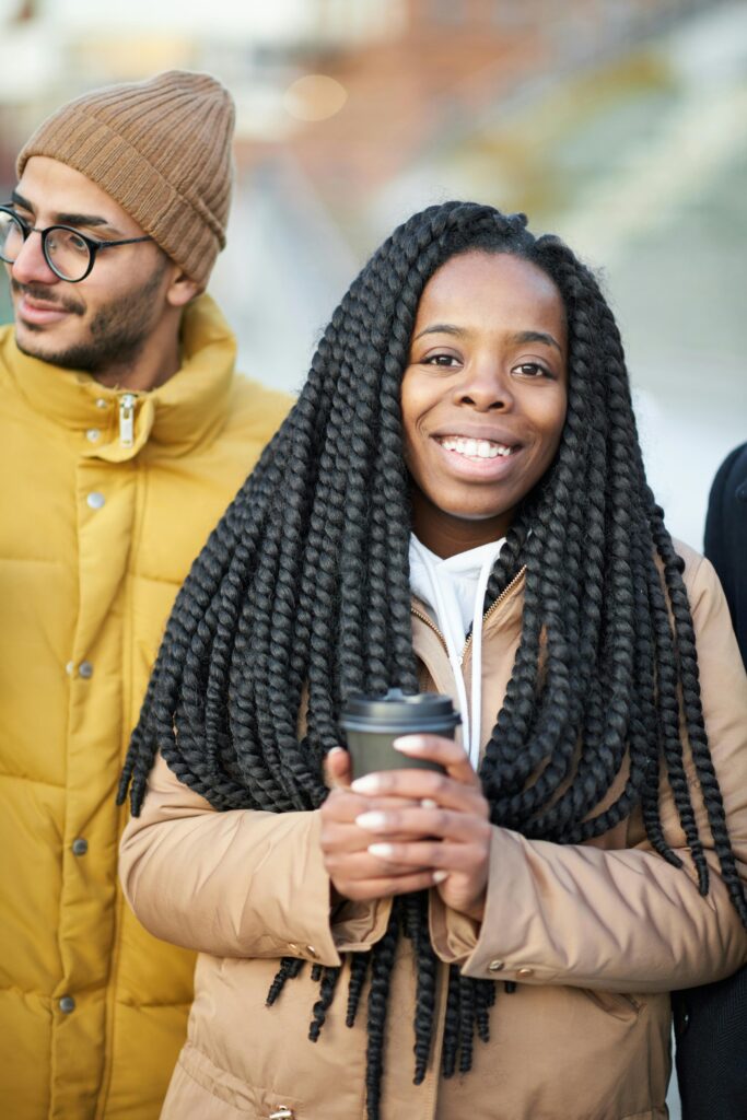Happy woman with braided hair holding a coffee cup in an outdoor setting.